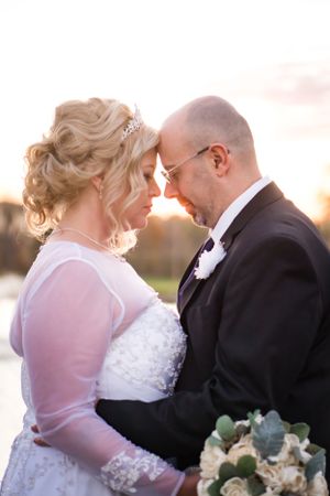 A romantic wedding portrait of a couple touching foreheads at sunset with a bridal bouquet.