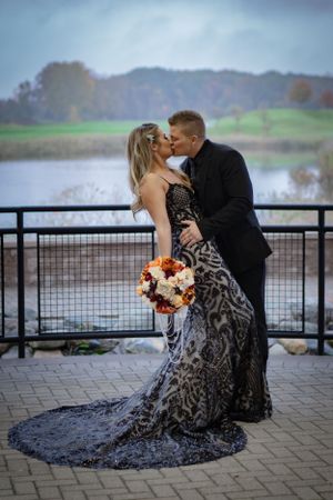Elegant couple in formal attire shares romantic moment on waterfront terrace.