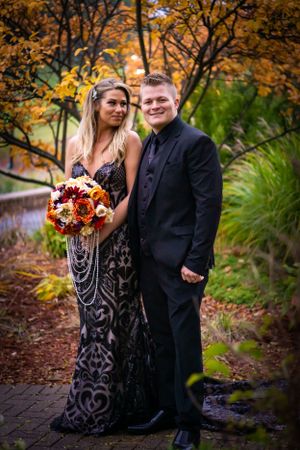 Formal couple poses with autumn foliage backdrop and vibrant bouquet.