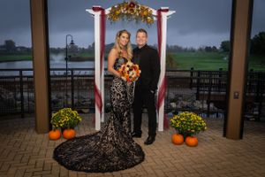 Formal couple poses by decorated arch with fall decorations and pumpkins.