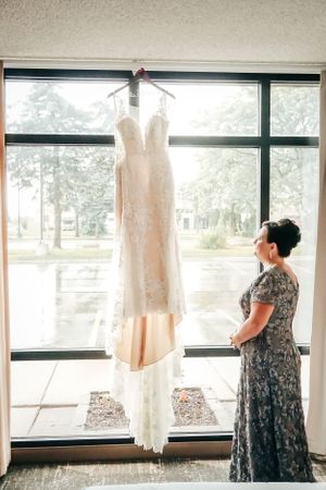 A wedding dress hangs elegantly in front of large windows while being admired.