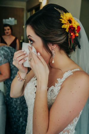 A bride with sunflower hair accessories wipes away tears while wearing a lace wedding dress.