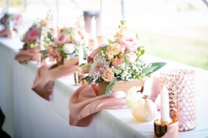 Delicate pink floral arrangements and candles decorate wedding reception table.