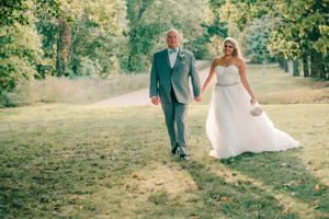 A couple walks through a sunlit park pathway during their wedding photoshoot.