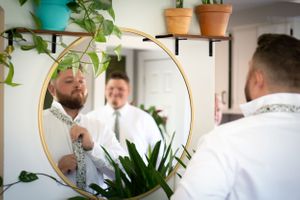 A circular mirror reflection shows wedding day preparations among potted plants.