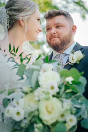 A romantic wedding photo with white roses and greenery in the foreground.