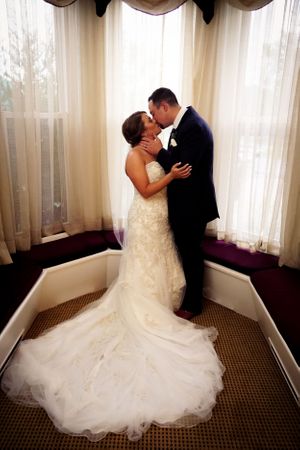 Romantic wedding portrait of couple embracing by window in elegant room.