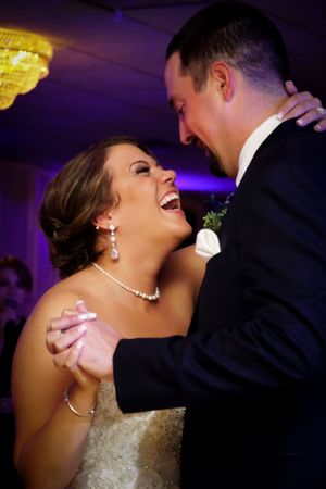 A joyful couple sharing a romantic dance moment under purple lighting at their wedding reception.