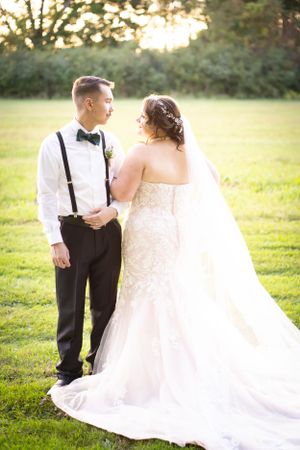 Wedding couple stands together in garden with bride wearing flowing lace gown and long veil.