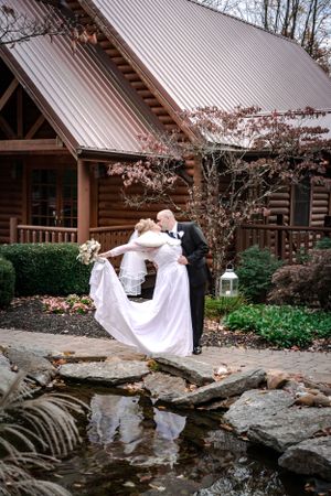 Romantic wedding photo in front of a rustic log cabin with water feature.