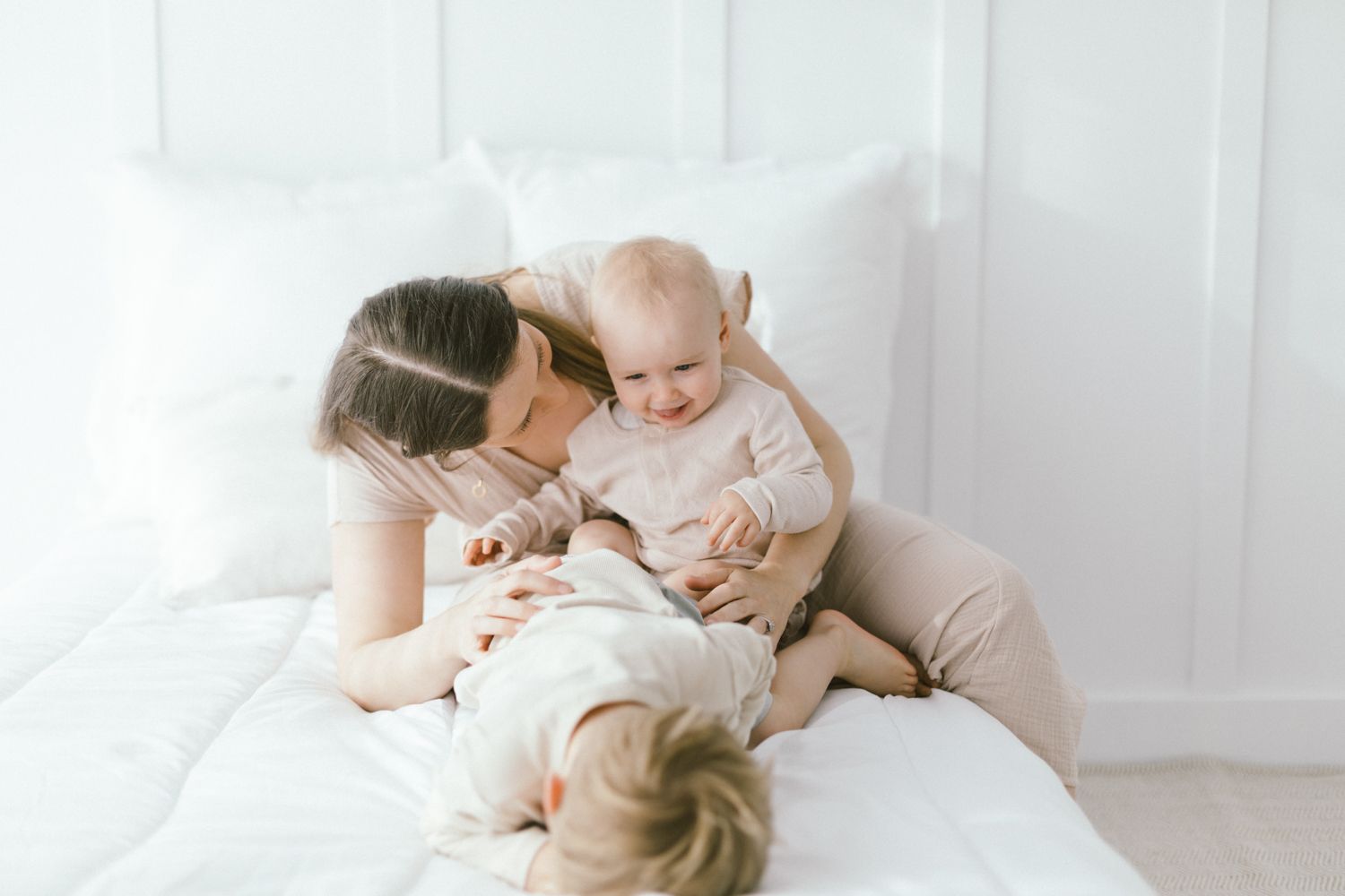 Intimate family portrait with soft embraces on white bedding.