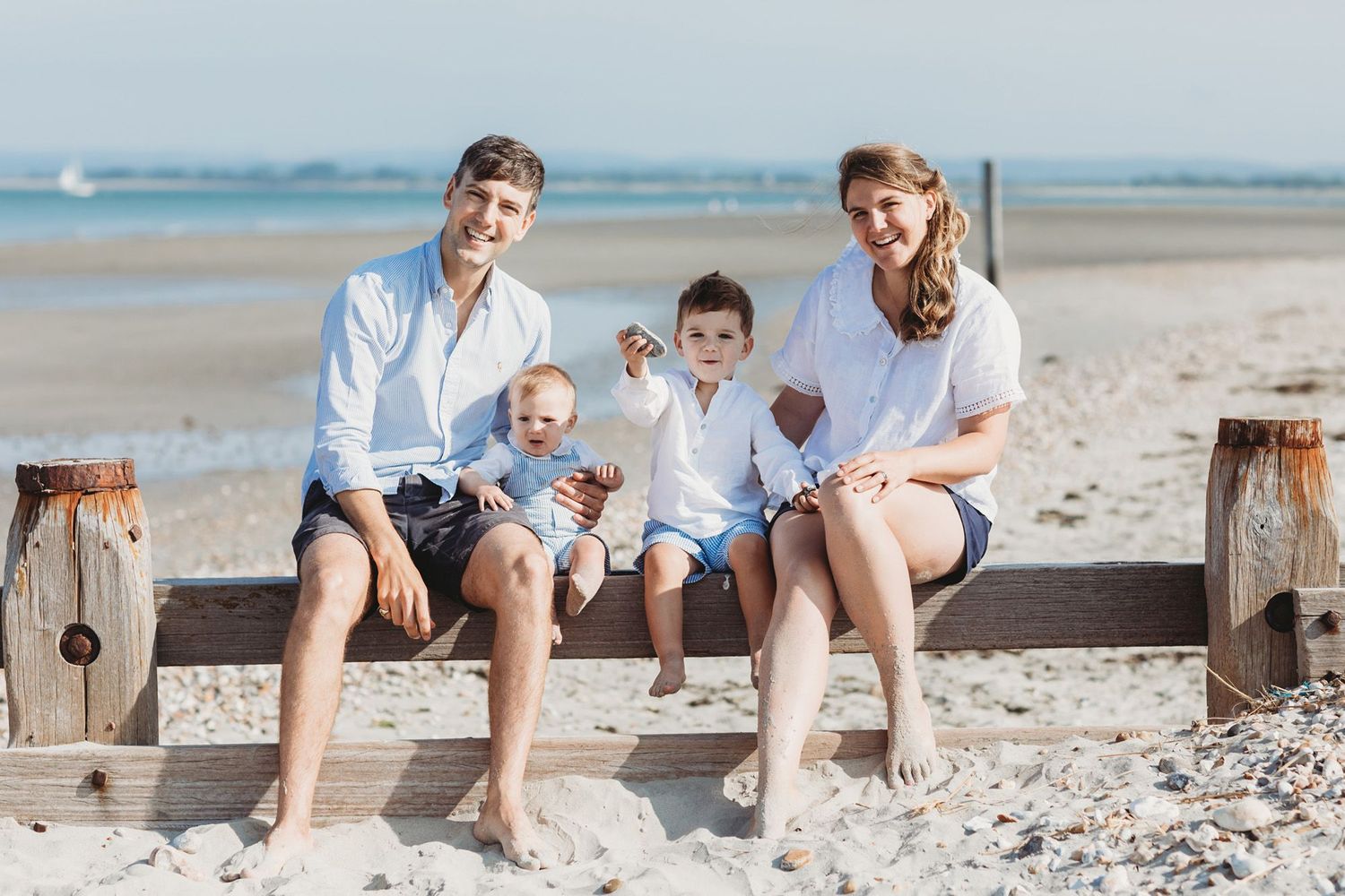 Casual family beach portrait on wooden bench with ocean view.