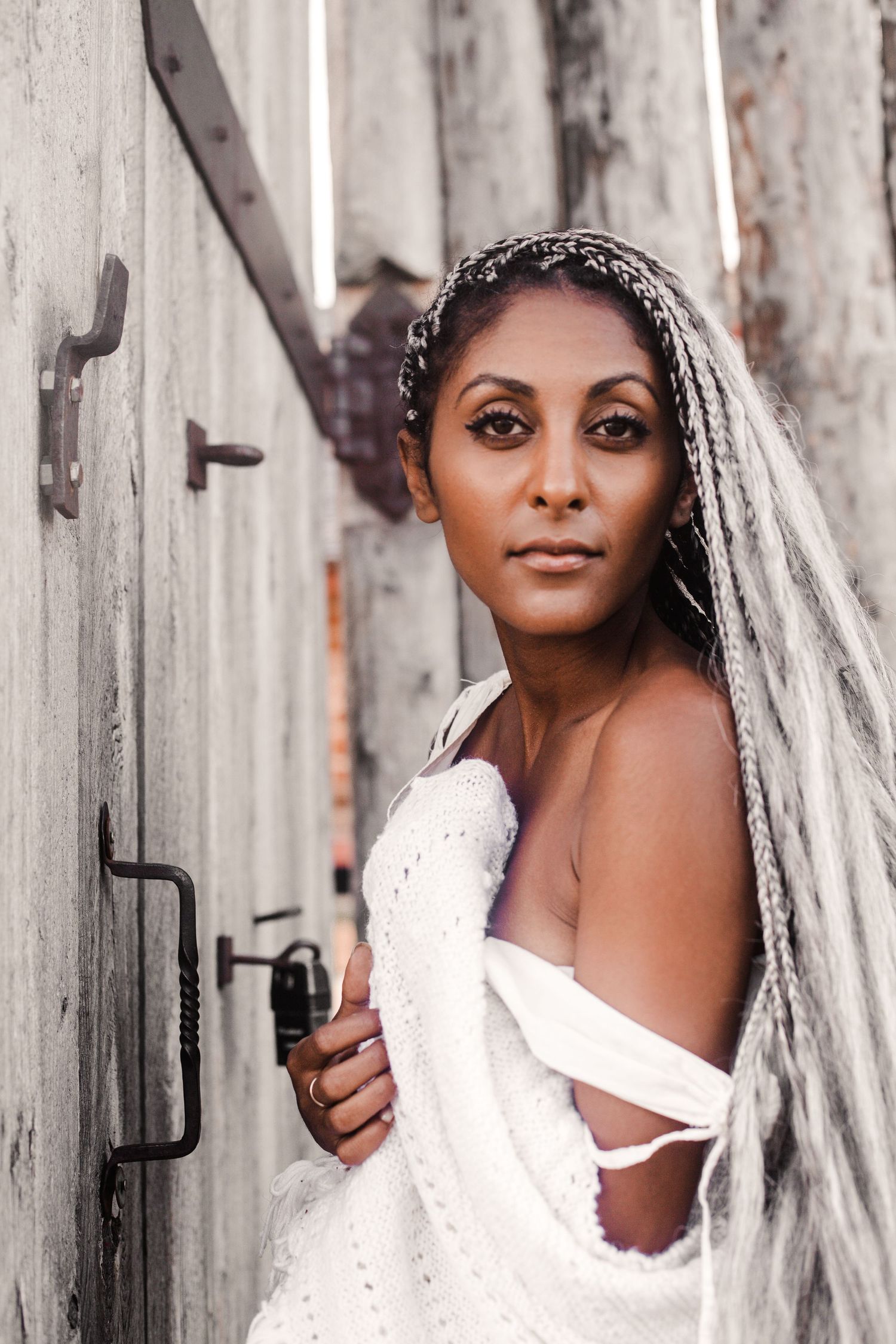 Elegant bride in white gown with long braided veil posing in a rustic alleyway doorway.