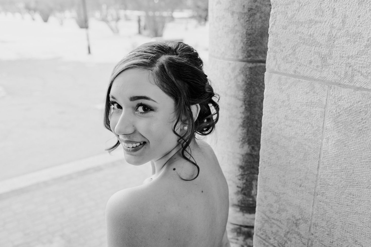 Elegant bride in updo hairstyle smiling over her shoulder in black and white portrait photo.