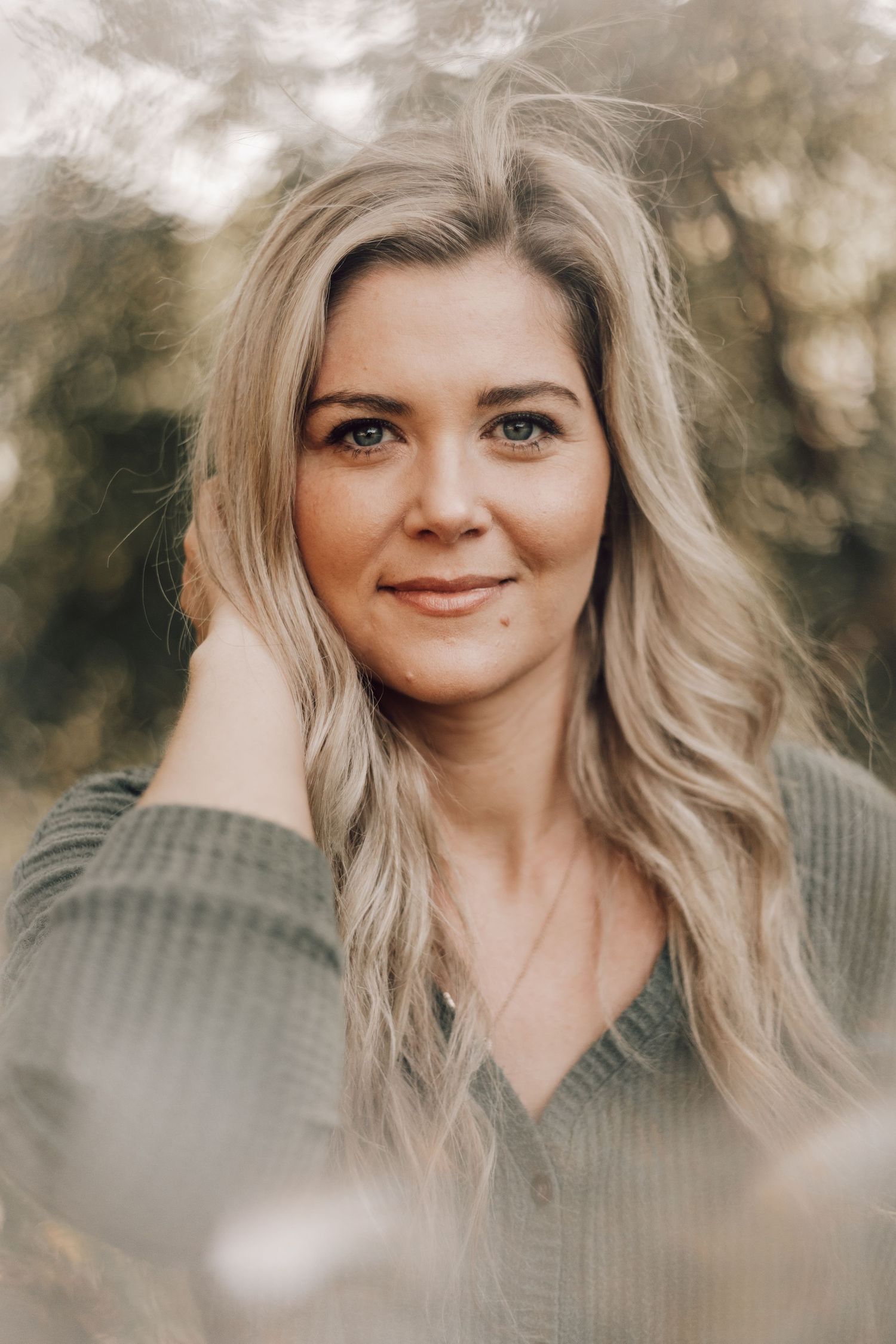 Close-up portrait of smiling blonde woman in green sweater with soft bokeh background.