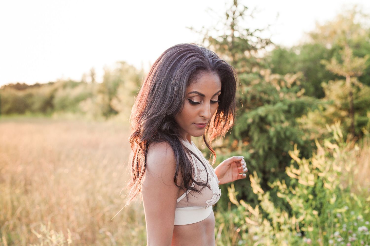 Young woman in white crop top standing in golden field at sunset with soft natural lighting.