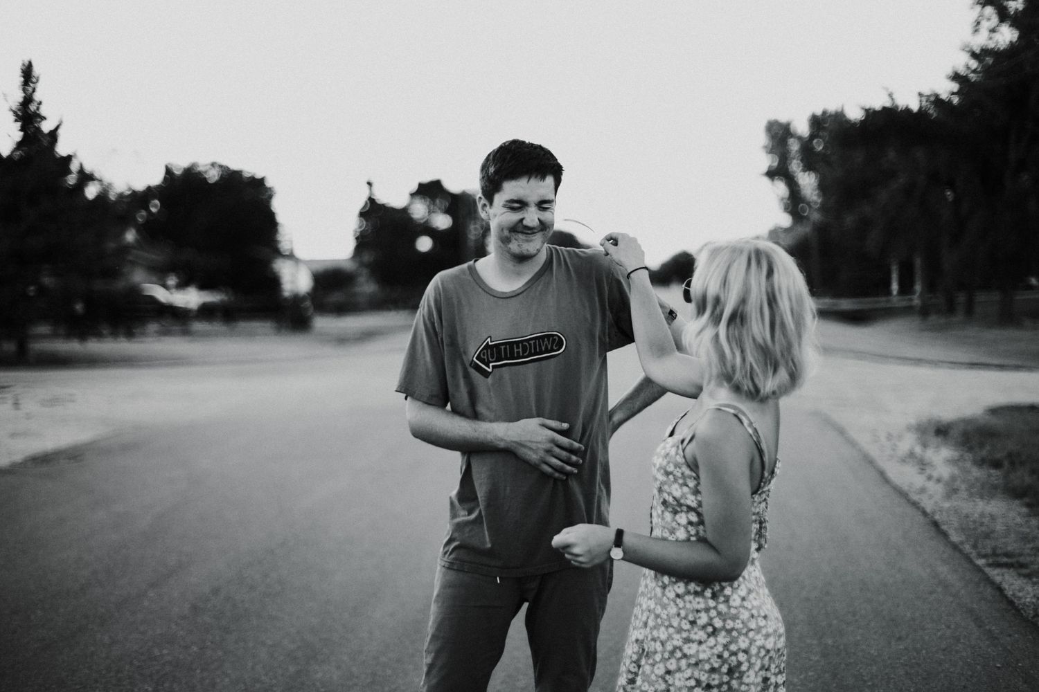 Young couple laughing together on an empty road surrounded by trees in black and white photo.