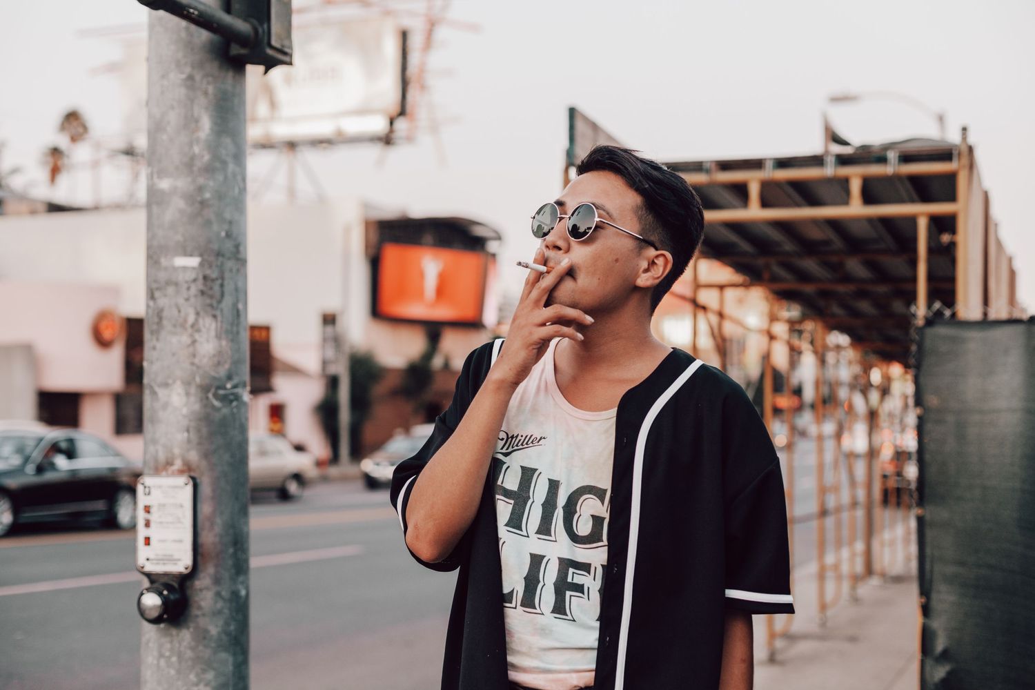 Stylish young man in sunglasses smoking a cigarette on a urban street wearing High Life tee.