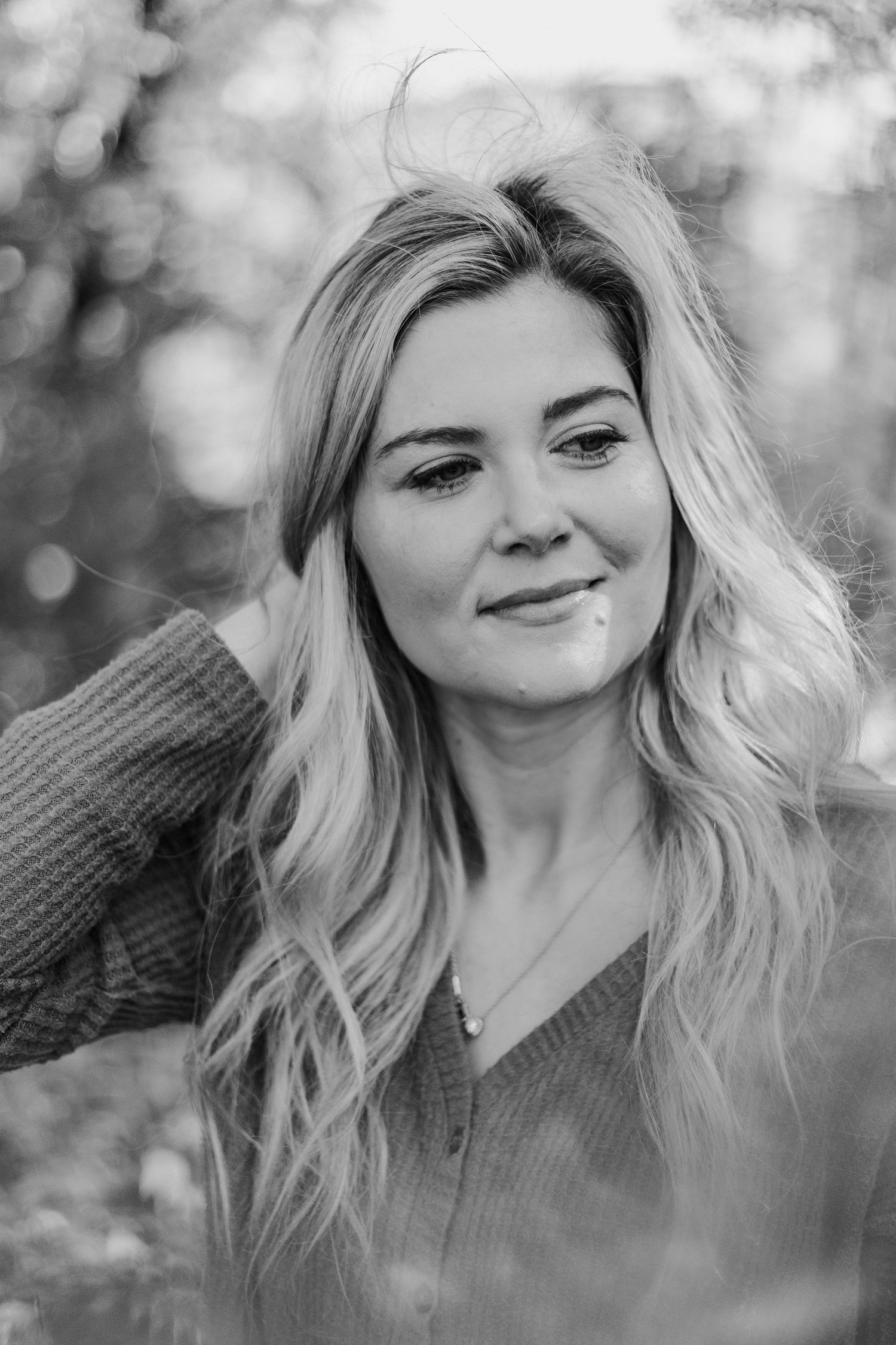 Black and white portrait of smiling blonde woman with long wavy hair outdoors.