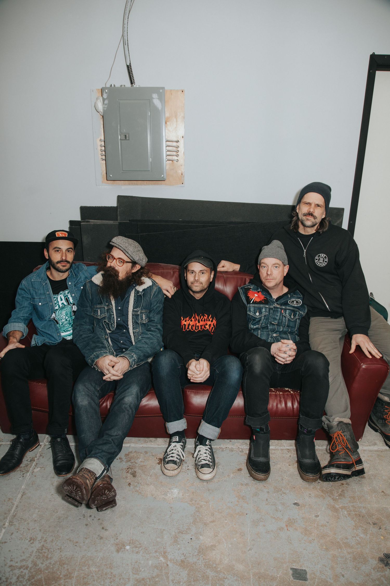 Five men sitting on a red leather couch in a casual band portrait photo.
