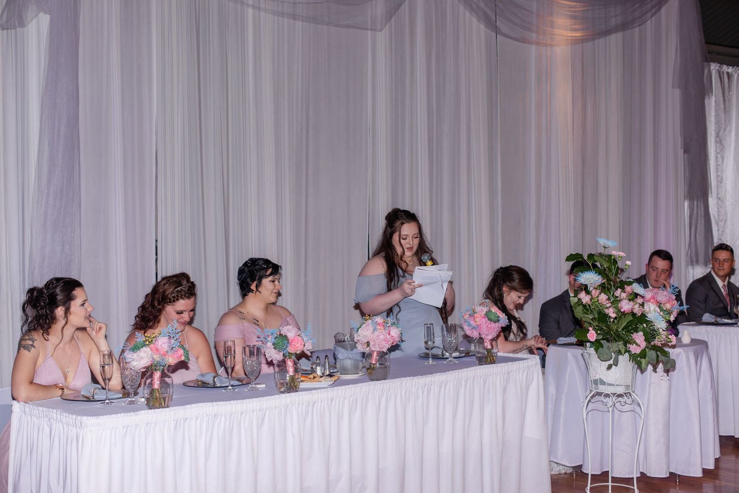 Long wedding reception head table decorated with floral arrangements and white linens.