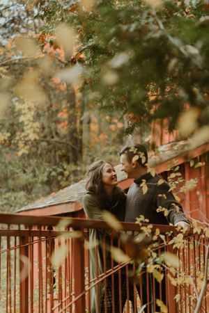Romantic couple sharing intimate moment on rustic red deck surrounded by autumn foliage.