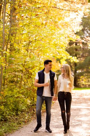 Couple walking and laughing together on autumn path surrounded by golden leaves.