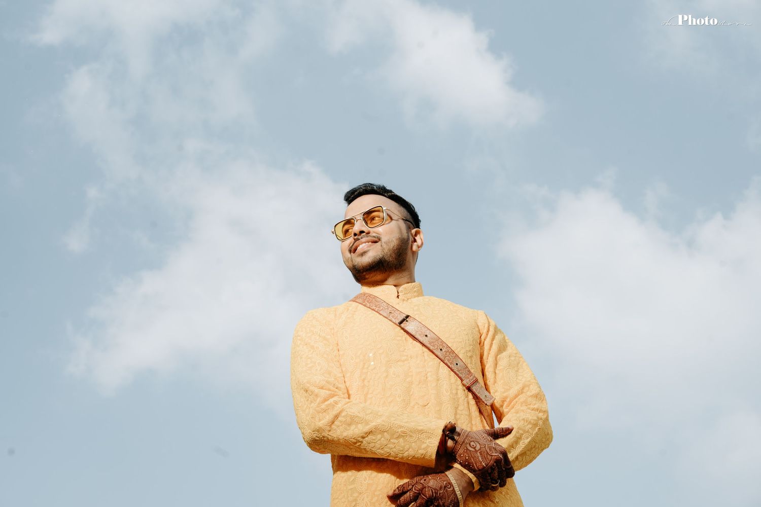Person in yellow formal attire poses against cloudy sky backdrop.