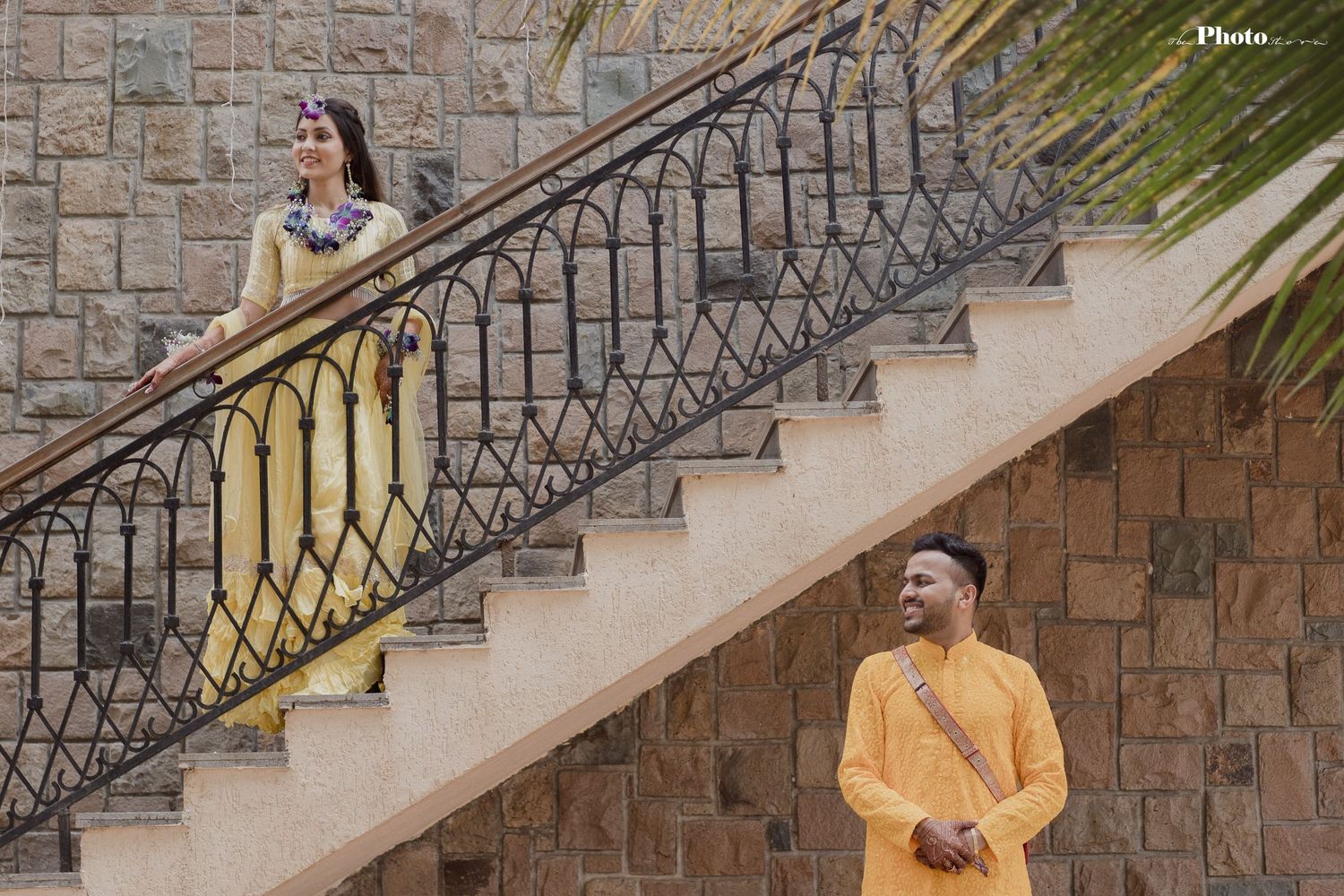 Person in yellow outfit stands on stone staircase with ornate metal railing.