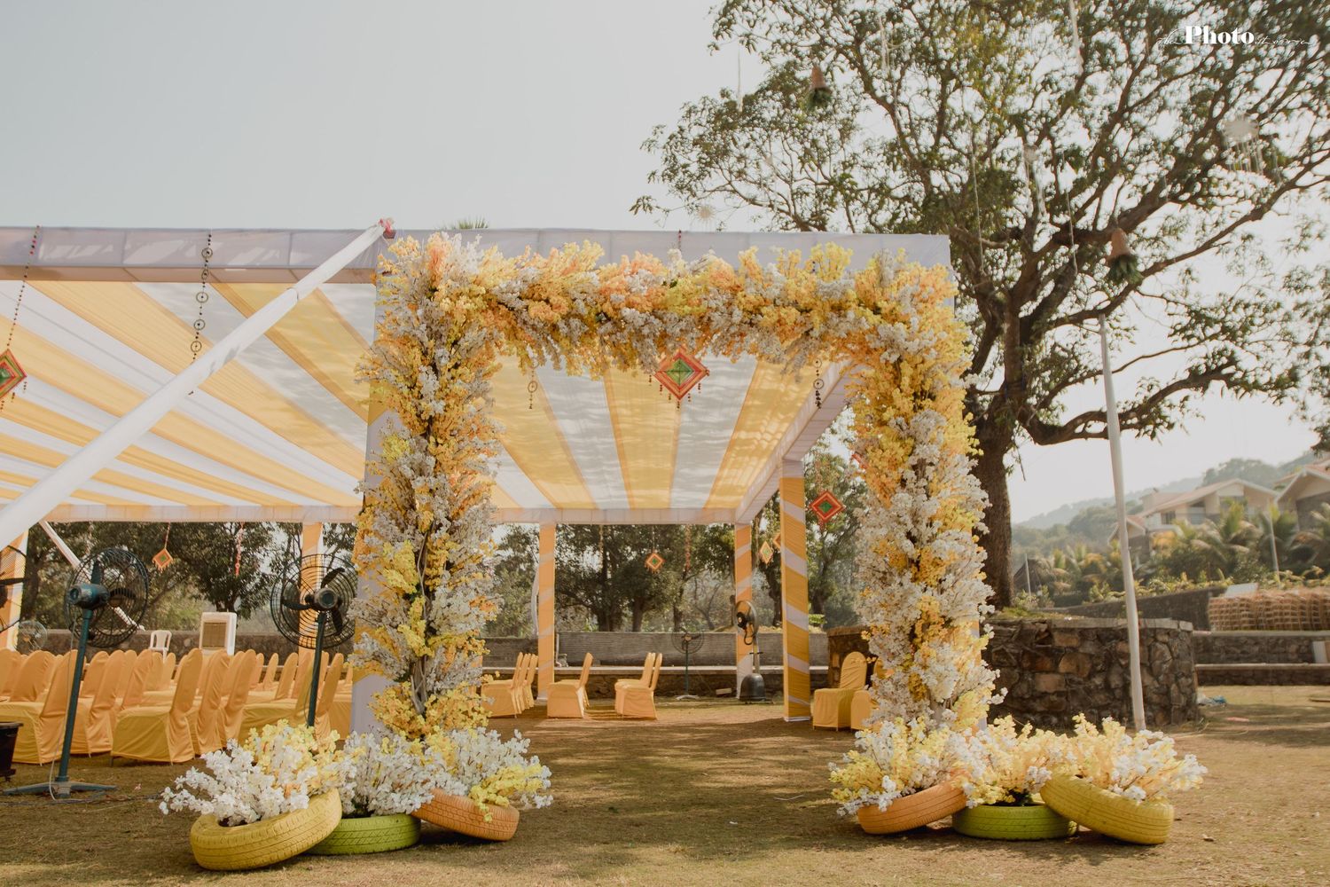 Wedding ceremony space decorated with white fabric and floral arrangements under trees.
