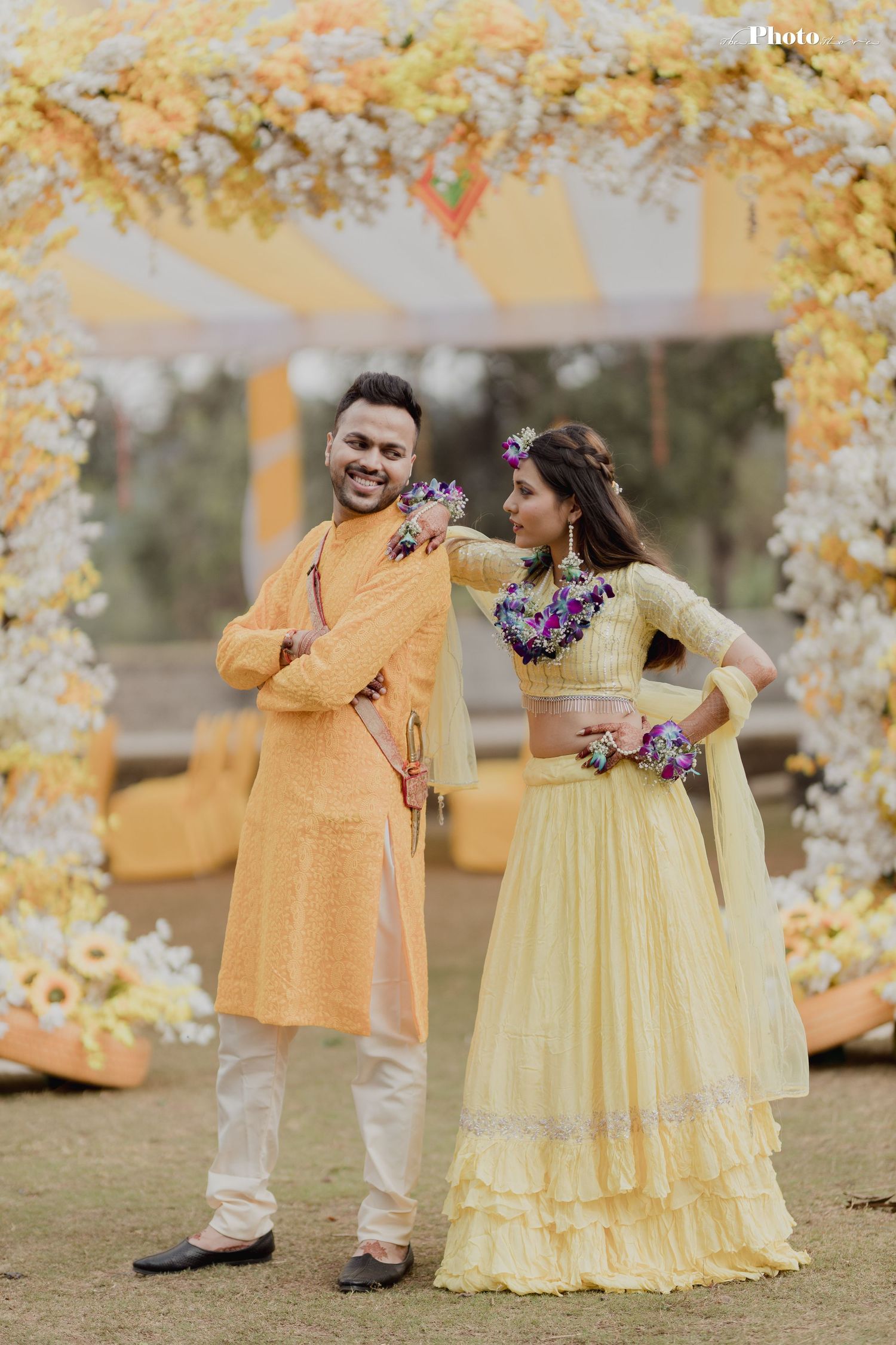 Couple in matching yellow outfits poses under floral arch during outdoor photoshoot.