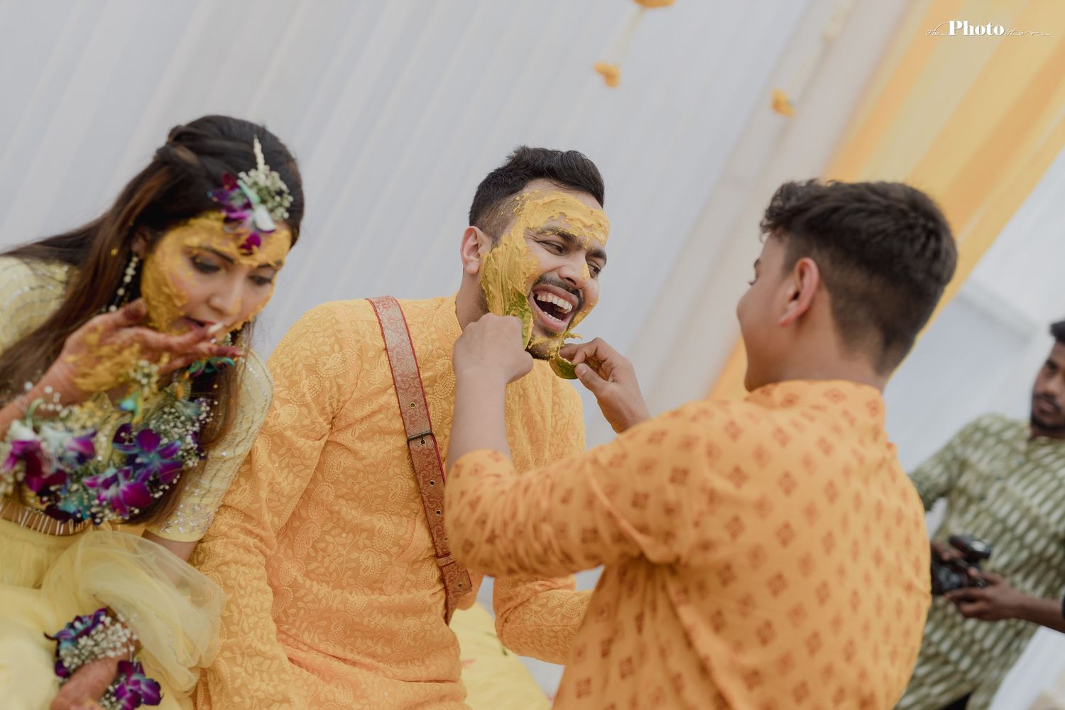 Playful moment during haldi ceremony with yellow turmeric being applied amidst laughter.