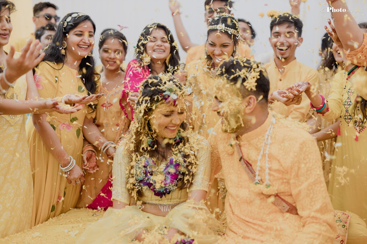 Group celebrates with flower petals during festive Indian wedding ceremony in yellow attire.