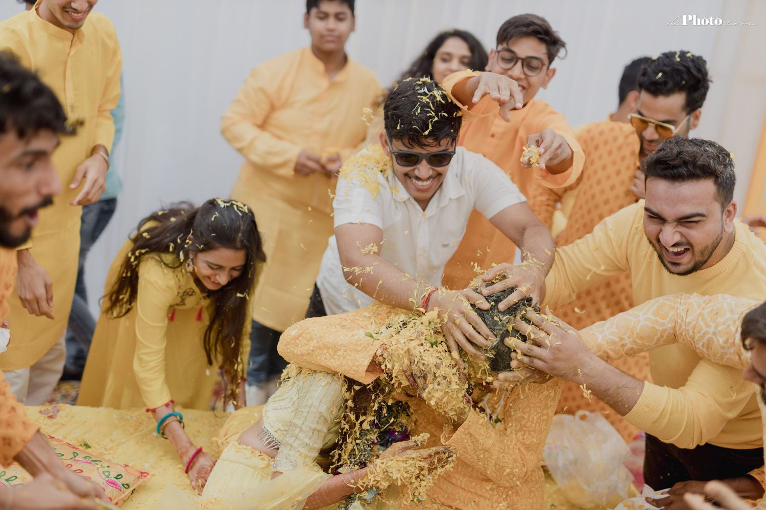Wedding guests in yellow traditional attire playfully throw turmeric powder during a Haldi ceremony celebration.
