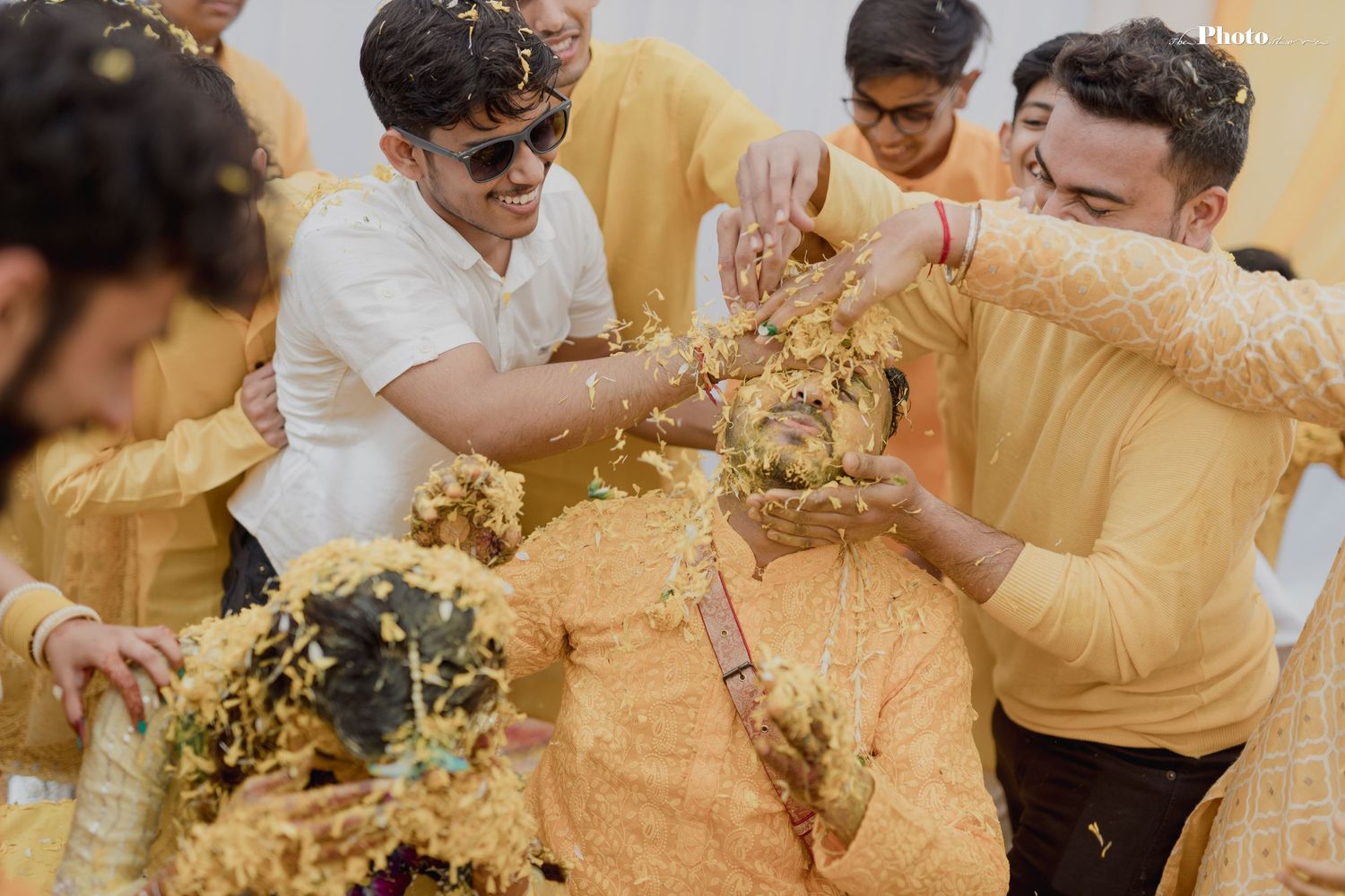 Joyful celebration at an Indian wedding ceremony with guests wearing yellow outfits throwing turmeric powder.