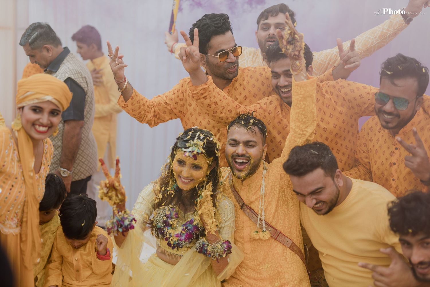 Festive group in yellow attire celebrates during a traditional Haldi ceremony with colorful powder.