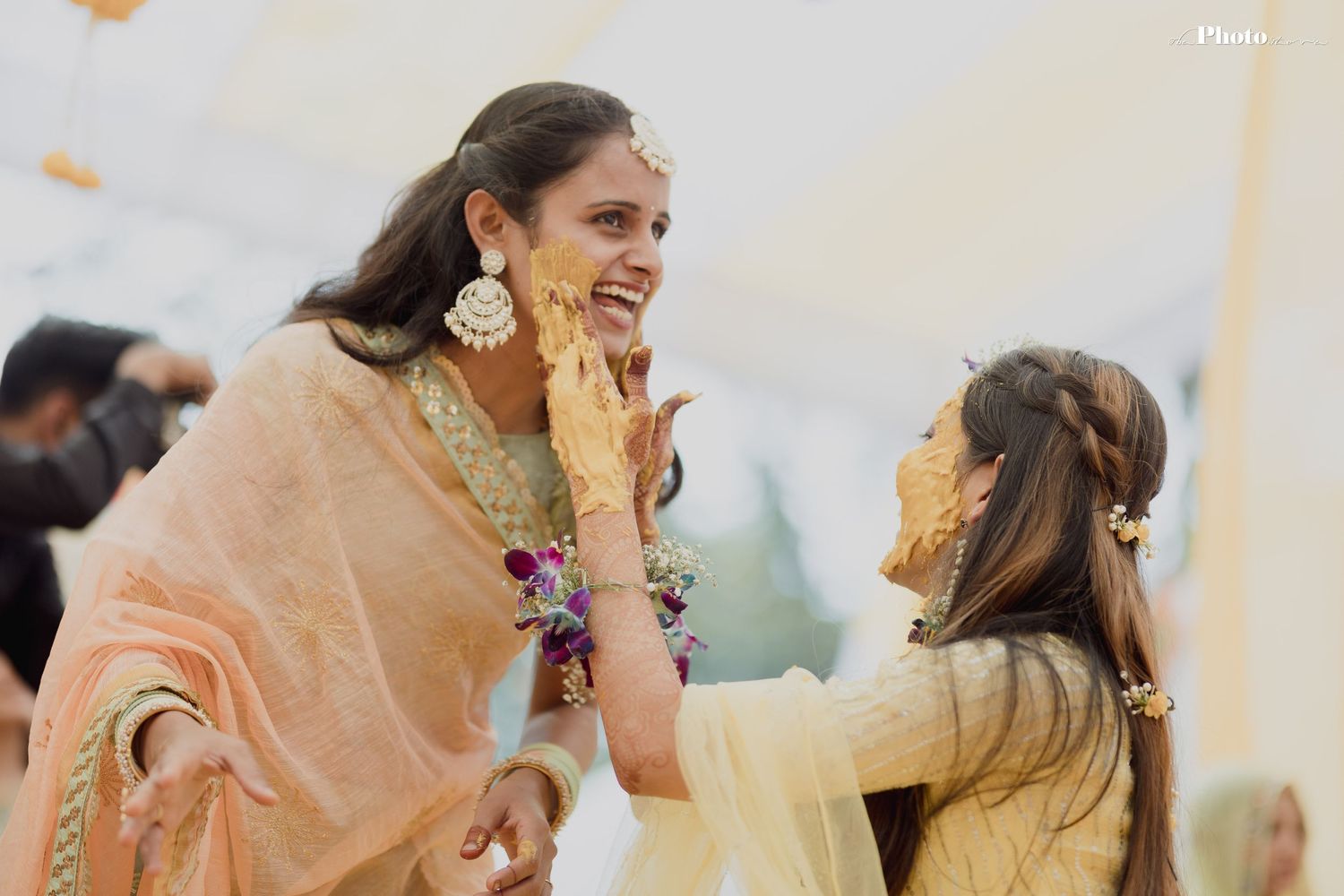Wedding party members in peach and yellow outfits share laughter during traditional ceremony.