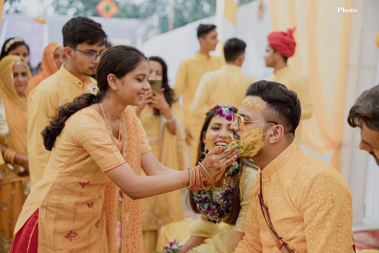Wedding party members in yellow outfits participate in a traditional haldi ceremony celebration.