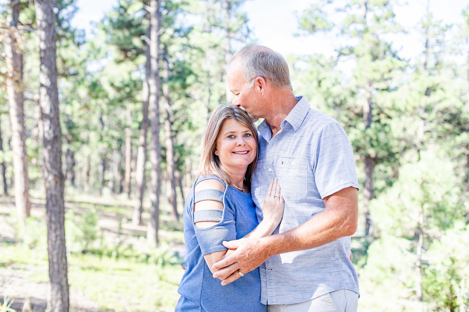 Husband kisses his wife's head as she smiles and hugs him in Black Forest, Colorado.