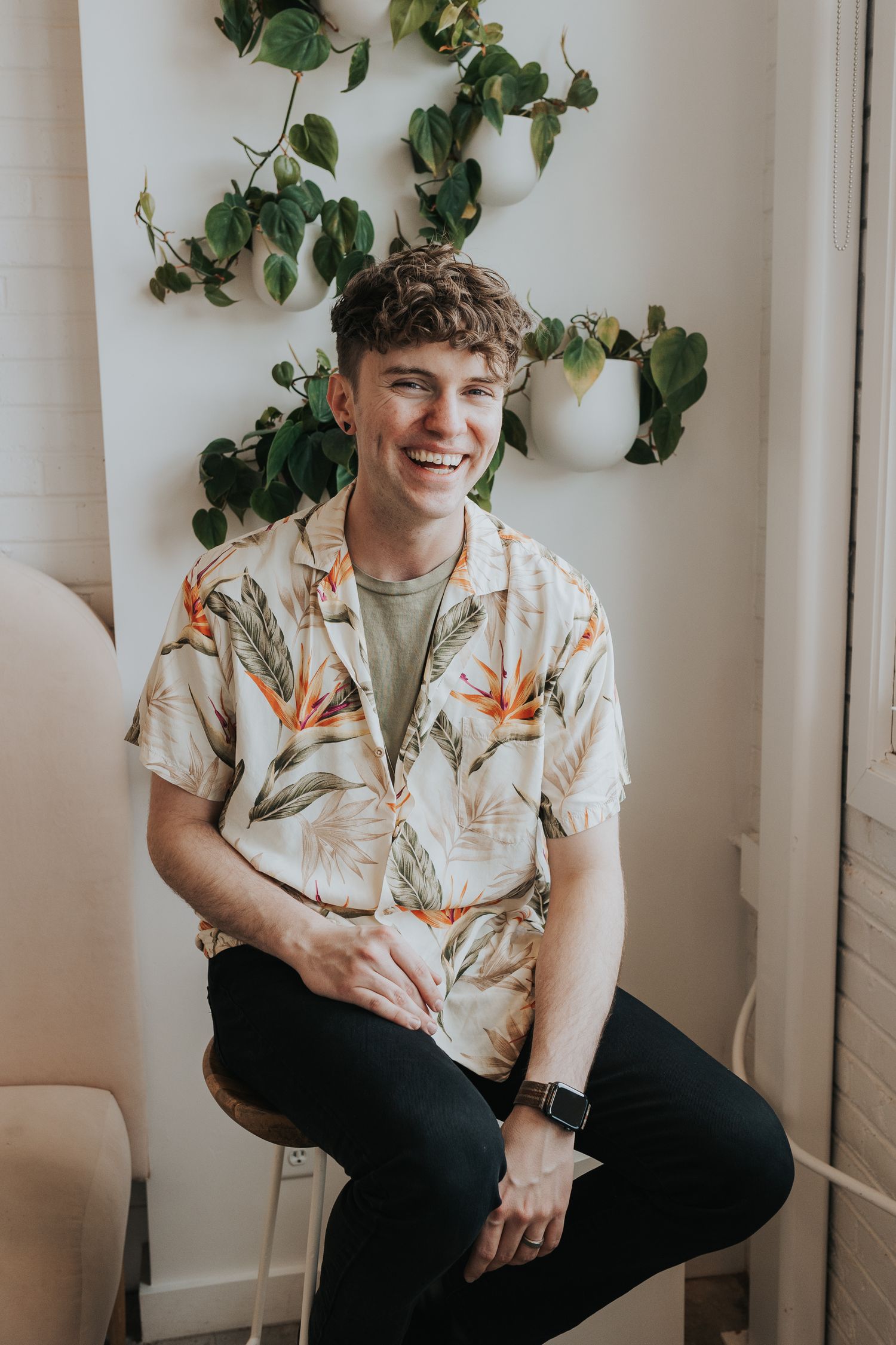 A casual portrait against white wall with hanging potted plants.