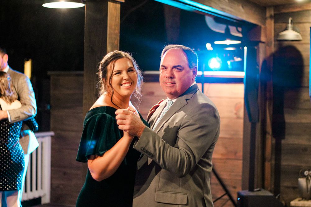 A father and daughter shares a dance under dim lighting in a rustic wooden venue.