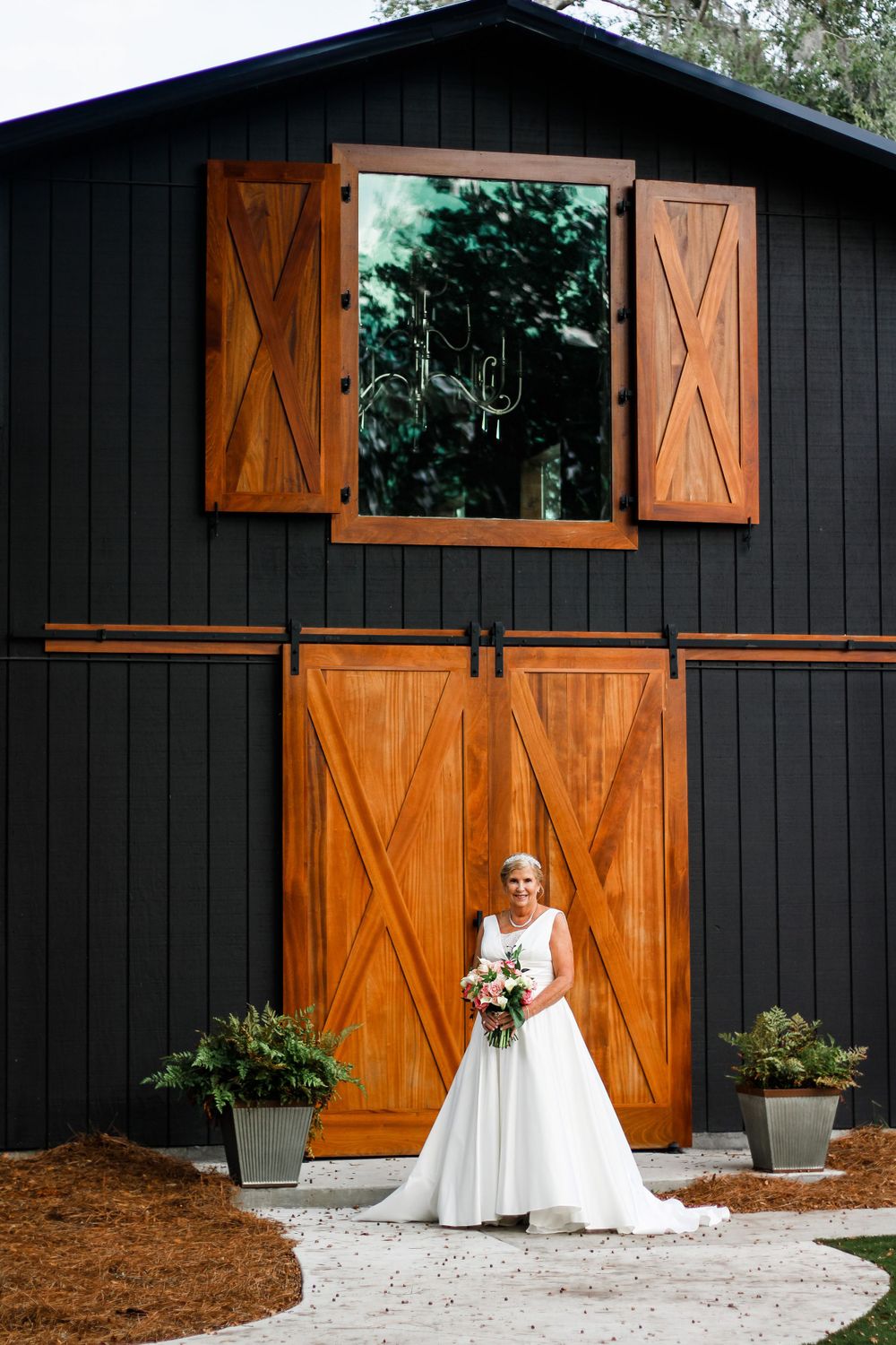 A bride in a white wedding gown poses in front of a modern black barn with orange wooden doors.