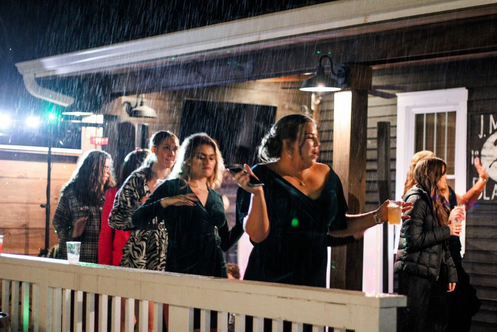 Guests enjoying a festive celebration on an outdoor porch in the rain at night.