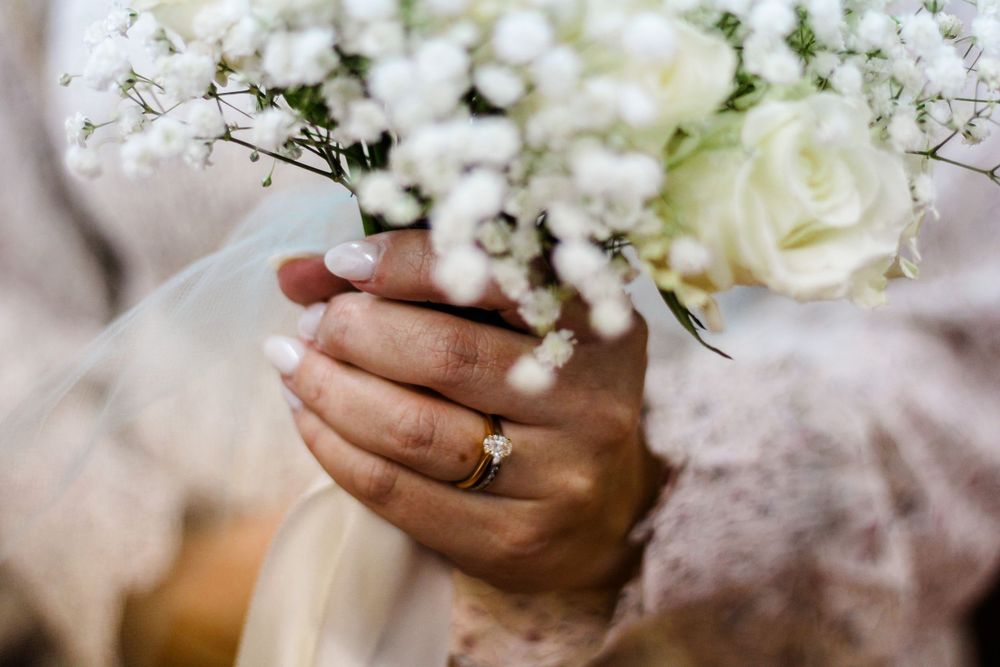 Close-up of hands holding white wedding bouquet with delicate flowers and wedding ring.