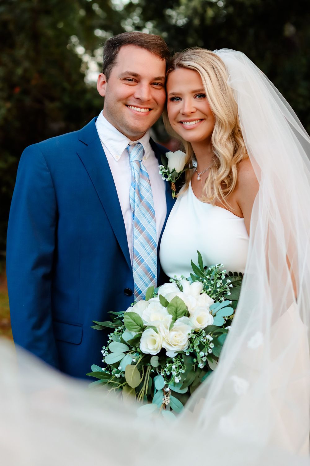 Happy newlyweds pose together with white bouquet and elegant attire.