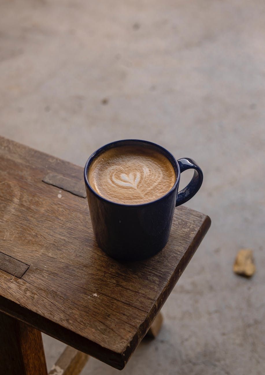 Black coffee mug with latte art heart design sitting on rustic wooden surface.