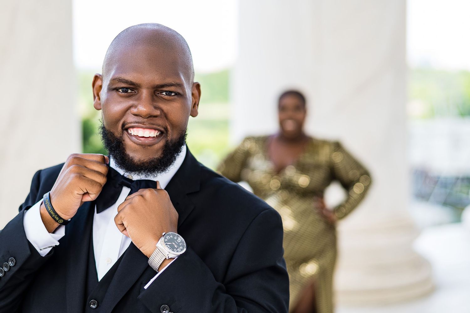 Well-dressed man in tuxedo smiles confidently by white columns.
