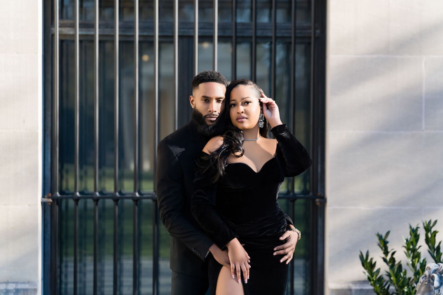Couple in black outfits poses fashionably against iron gate.