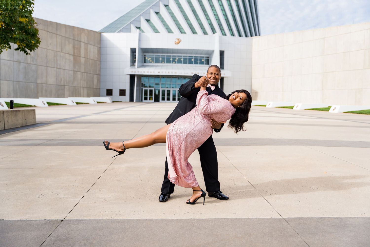 Couple performs dramatic dance dip pose outside modern building.