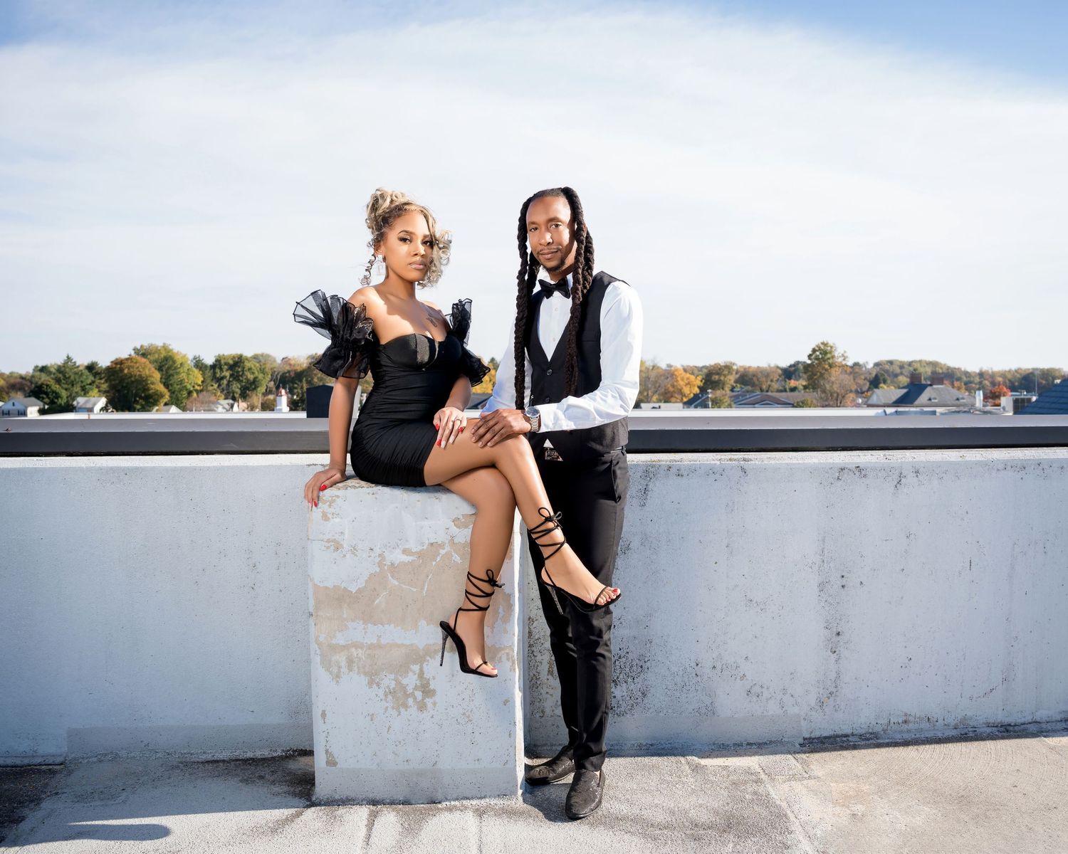 Stylish couple in formal attire poses on urban rooftop.